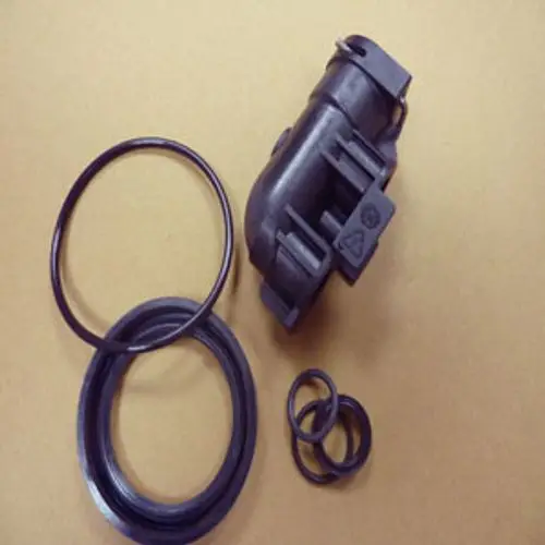 Anschlusstück der Marke Remeha mit mehreren O-Ringen, abgebildet auf einer braunen Unterlage. Das Teil hat eine komplexe Form und dient zur Verbindung in einem System.
